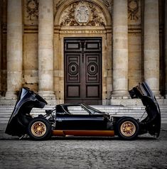 two black and gold cars parked in front of a large building with columns on either side