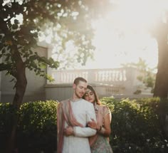 a man and woman standing next to each other in front of some trees with the sun shining on them