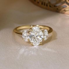 a three stone diamond ring sitting on top of a white cloth covered table next to a gold vase