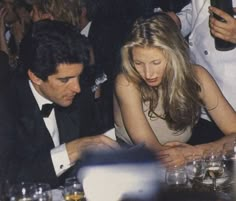 a man and woman sitting at a table with drinks in front of them, looking down