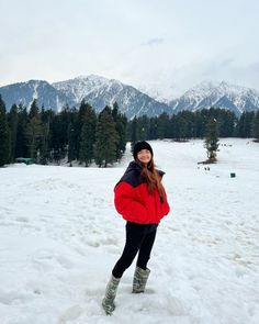 a woman is standing in the snow with her hands on her hips and mountains in the background