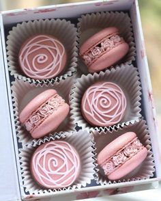 four pink macaroons in a box with swirl designs on the outside and inside