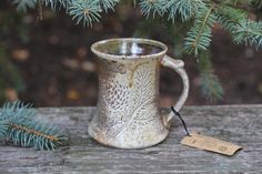 a mug sitting on top of a wooden table next to a pine tree with a tag