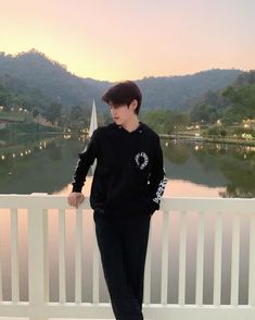 a young man standing on top of a white fence next to a body of water