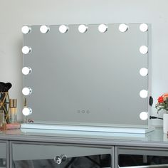 a vanity mirror with lights on top of it next to a vase and flower pot