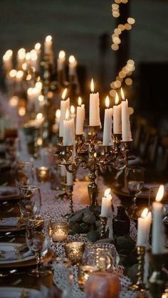 a long table with many lit candles on it and place settings in front of them