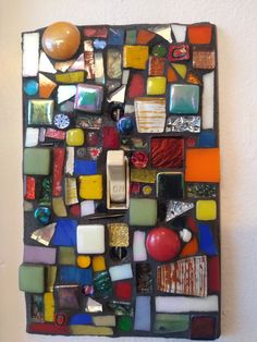 a multicolored glass and metal wall hanging on a white wall with a light switch