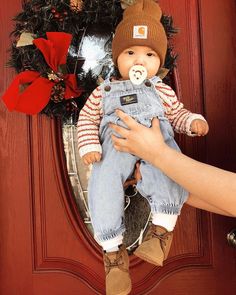 a person holding a baby doll in front of a door with christmas wreaths on it