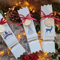 three christmas crackers are tied with red ribbon and decorated with pine cones, holly berries, and gold ornaments