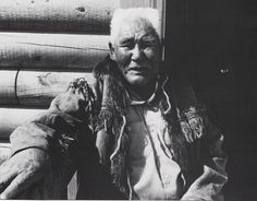 an old native american man sitting in front of a pile of logs with his hands on his hips