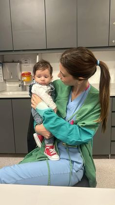 a woman holding a baby in her arms while sitting on a counter top next to a sink