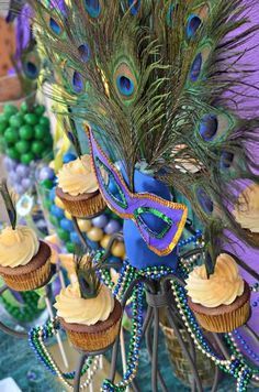 peacock feathers and cupcakes are on display at a mardi gras party