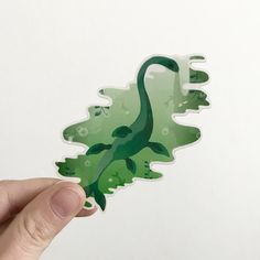 a hand holding up a green sticker with a lizard on it