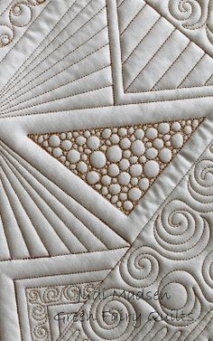 a close up view of a quilt with white and gold threadwork on the edges