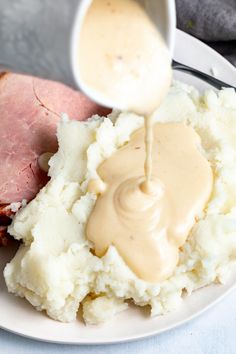 a plate with mashed potatoes, ham and gravy on it is being poured over the top