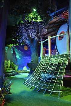 an indoor playground with slides and trees in the background