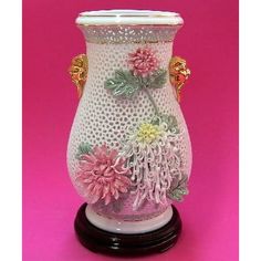 a white vase with pink and yellow flowers on the inside is sitting on a black stand