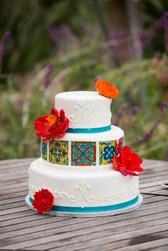 a three tiered white cake with red flowers on the top and blue trimmings