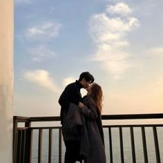 a man and woman standing next to each other on a balcony near the ocean kissing