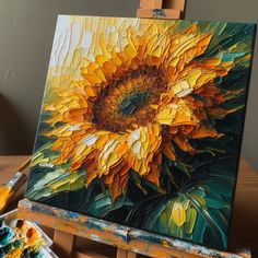 an oil painting of a yellow sunflower on a easel next to some paintbrushes