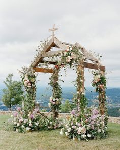 a wooden structure with flowers and greenery around it on the top of a hill