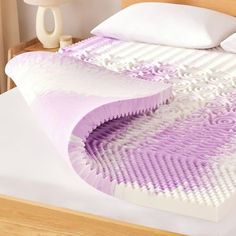 the bed is made up with purple and white designs on it's sides, along with two pillows