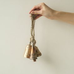 a hand is holding two bells that are hanging from the side of a white wall