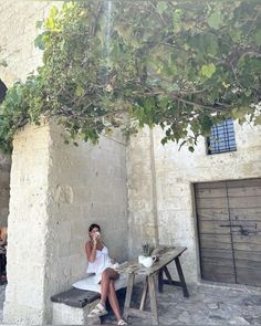 a woman sitting on a bench talking on her cell phone in front of a building