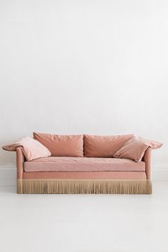 a pink couch with two pillows on the back and one pillow on the side, in front of a white wall