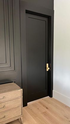 an empty room with black walls and wooden flooring is pictured in this image, there is a chest of drawers next to the door