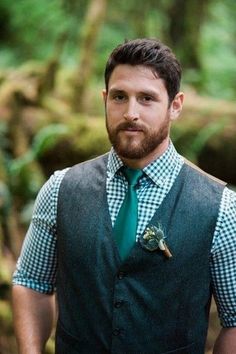 a man with a beard wearing a green tie and vest in the middle of a forest