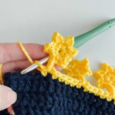 someone is crocheting flowers on the side of a blue knitted object with a green crochet hook