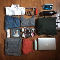 an assortment of clothing and accessories laid out on a wooden floor next to a laptop