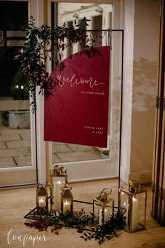 candles are arranged on the floor in front of a red welcome sign with greenery