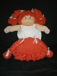 a doll with red hair and blue eyes sitting on a black cloth covered surface in front of a black background