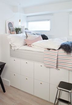 a bed with pillows and blankets on top of it next to a desk in front of a window