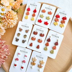 six pairs of earrings with autumn leaves and mushrooms on them sitting on a table next to flowers