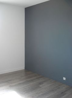 an empty room with gray walls and wood flooring is seen in this image from the corner