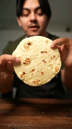 a man holding up a tortilla on top of a wooden table