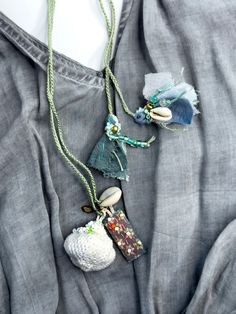 a woman wearing a gray shirt with some necklaces on her neck and two seashells hanging from it