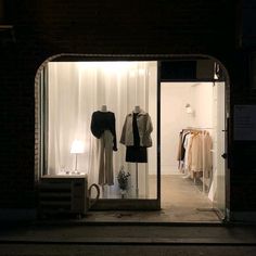 an open window with clothes on display in the front and side windows lit up at night