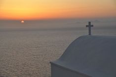 a cross on top of a steeple with the sun setting in the distance behind it