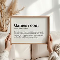 a person holding up a framed sign that says games room in front of a white couch