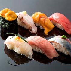 four sushi rolls with different toppings are arranged on a black surface