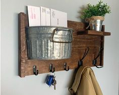 a metal bucket and some keys hanging on a wooden shelf above a coat rack with hooks