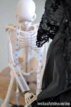 a skeleton sitting on top of a wooden table next to a black cloth covered doll