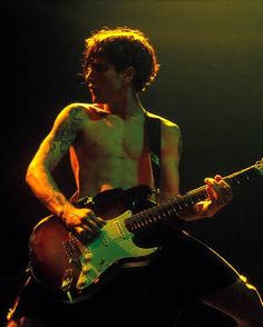 a shirtless man playing an electric guitar on stage