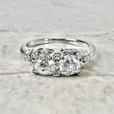 three stone diamond ring sitting on top of a white marble surface with two diamonds in the middle