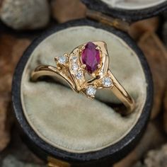 a gold ring with an oval shaped ruby stone surrounded by small white diamonds in a velvet box