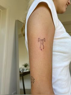 a woman's arm with a bow tattoo on the left side of her arm